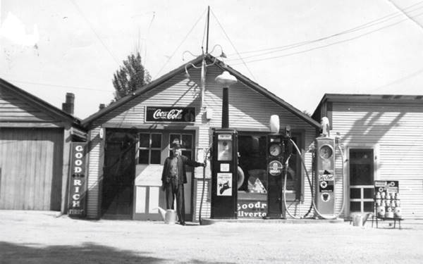 black and white 1920s, man by 3 Texaco pumps, a gas station gable roof, no canopy, woodframe